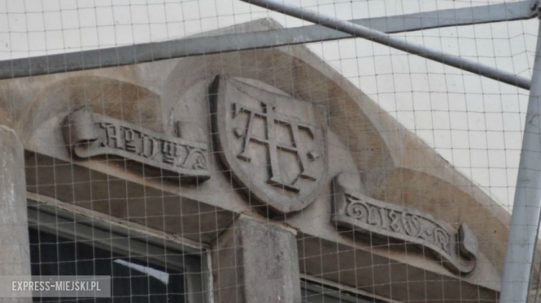Inicjały architekta planującego ząbkowicki ratusz – Alexis Langer był niemieckim architektem uwielbiającym gotyk. Gdy w 1860 roku otrzymał zgodę na odbudowę spalonego ratusza ochoczo wziął się za szkice fasady. Budowę ukończył w dwa lata (1862-1864). Żeby zaznaczyć, że projekt był jego autorstwa, nad głównym wejściem do ratusza umieścił w herbie swoje inicjały. Podobne znaki możemy znaleźć na innych budynkach jego autorstwa, m.in. na kościele w Bielawie oraz Wrocławiu